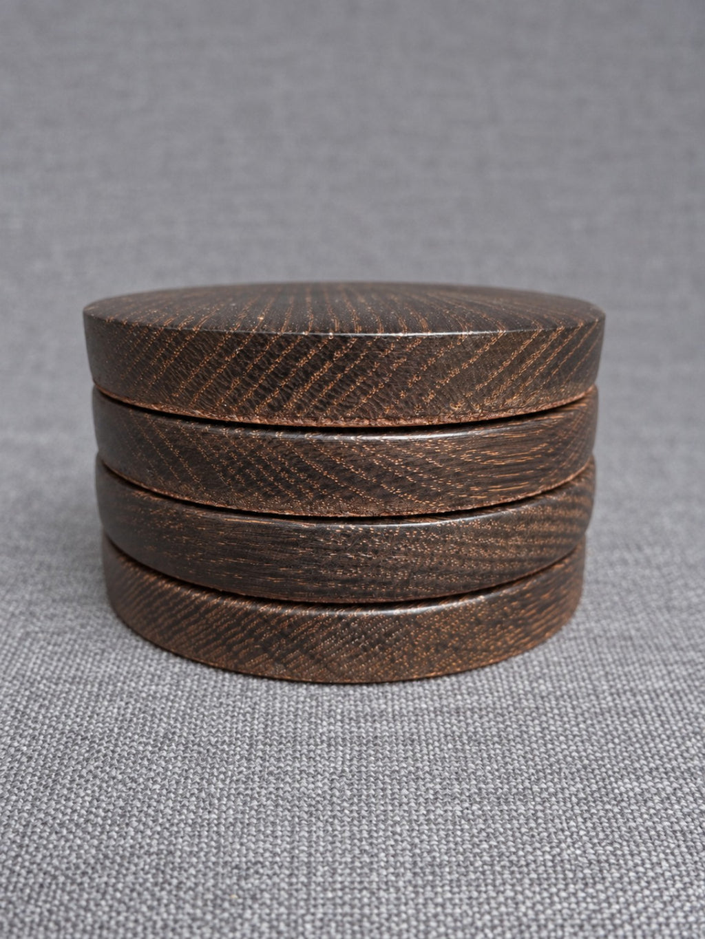 Four bronze grain ebonised oak coasters stacked on grey fabric