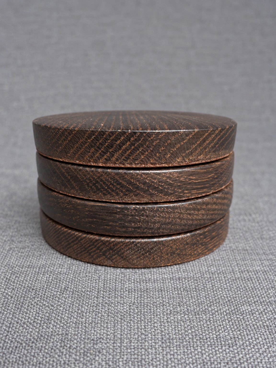 Four bronze grain ebonised oak coasters stacked on grey fabric