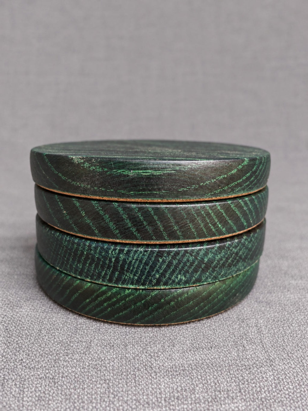Stacked ebonised oak coasters with green highlighted grain