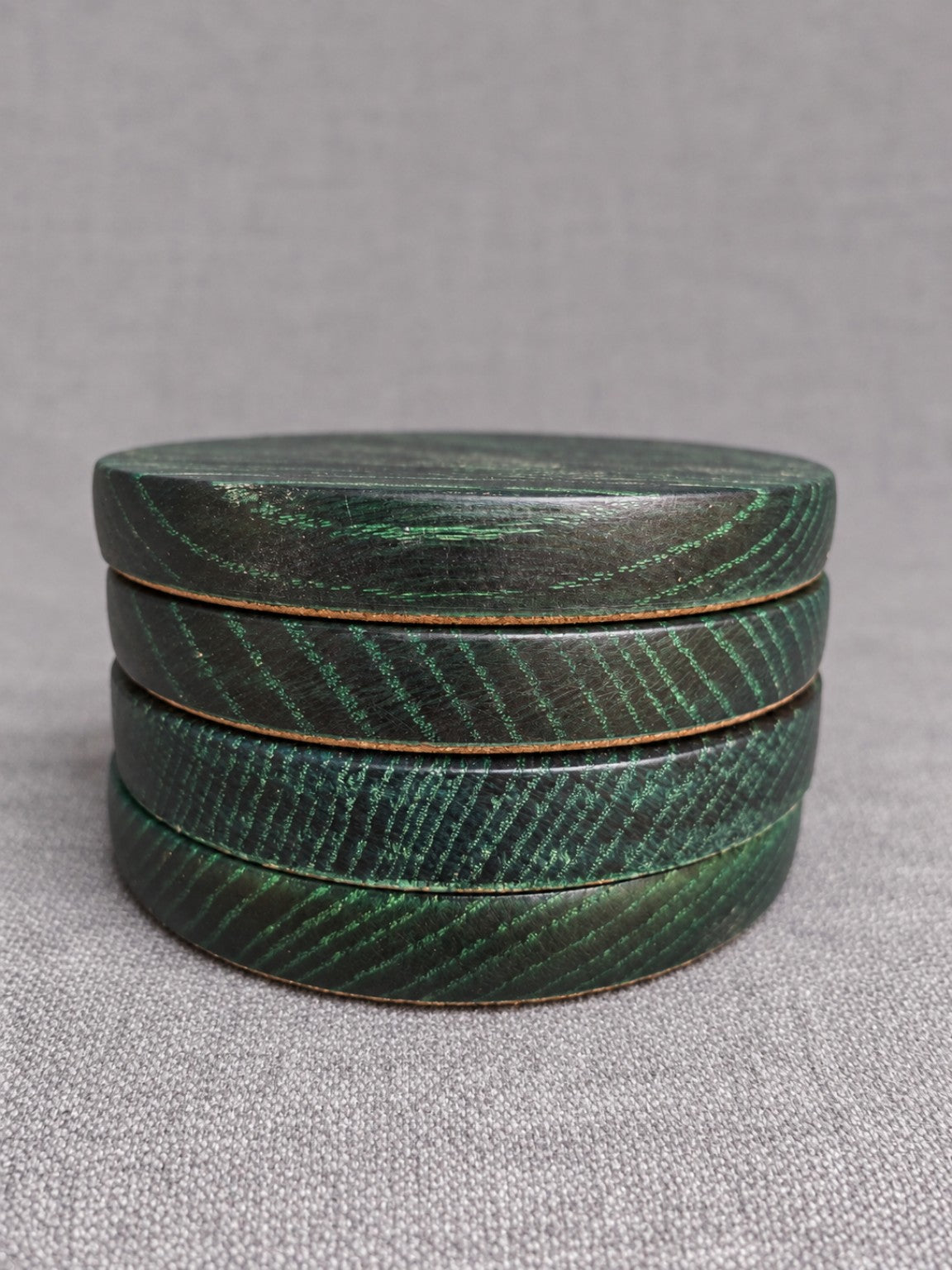 Stacked ebonised oak coasters with green highlighted grain