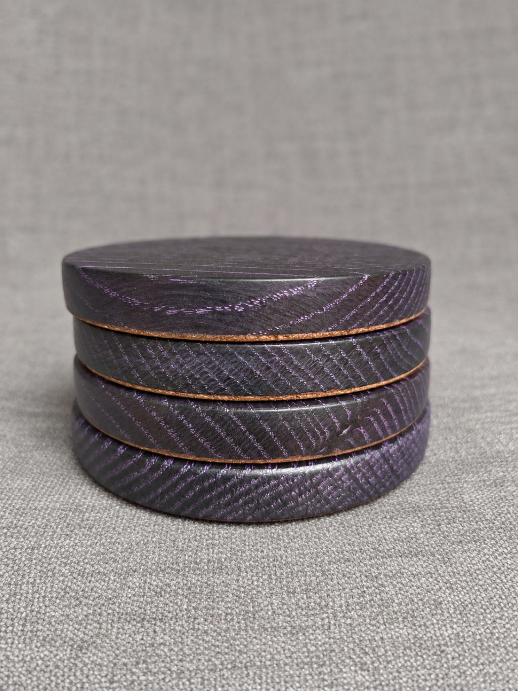 Stacked ebonised oak coasters with purple highlighted grain