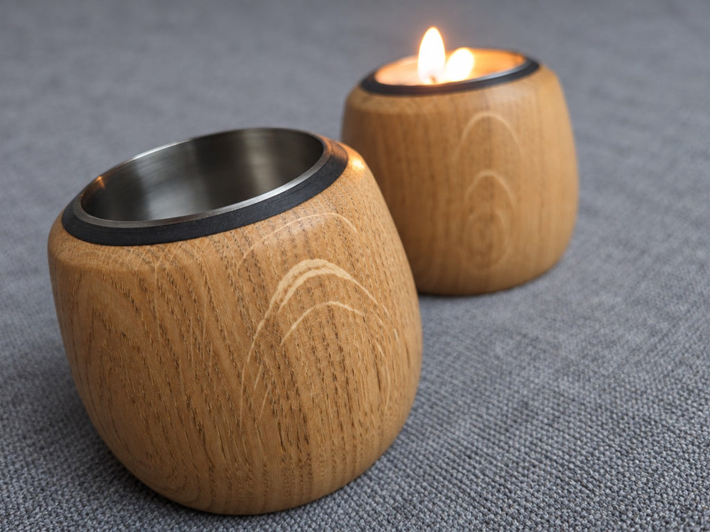 Pair of oak tealight holders with a candle lit in the rear holder and pale flecking in the foreground grain