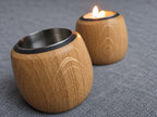 Pair of oak tealight holders with a candle lit in the rear holder and pale flecking in the foreground grain