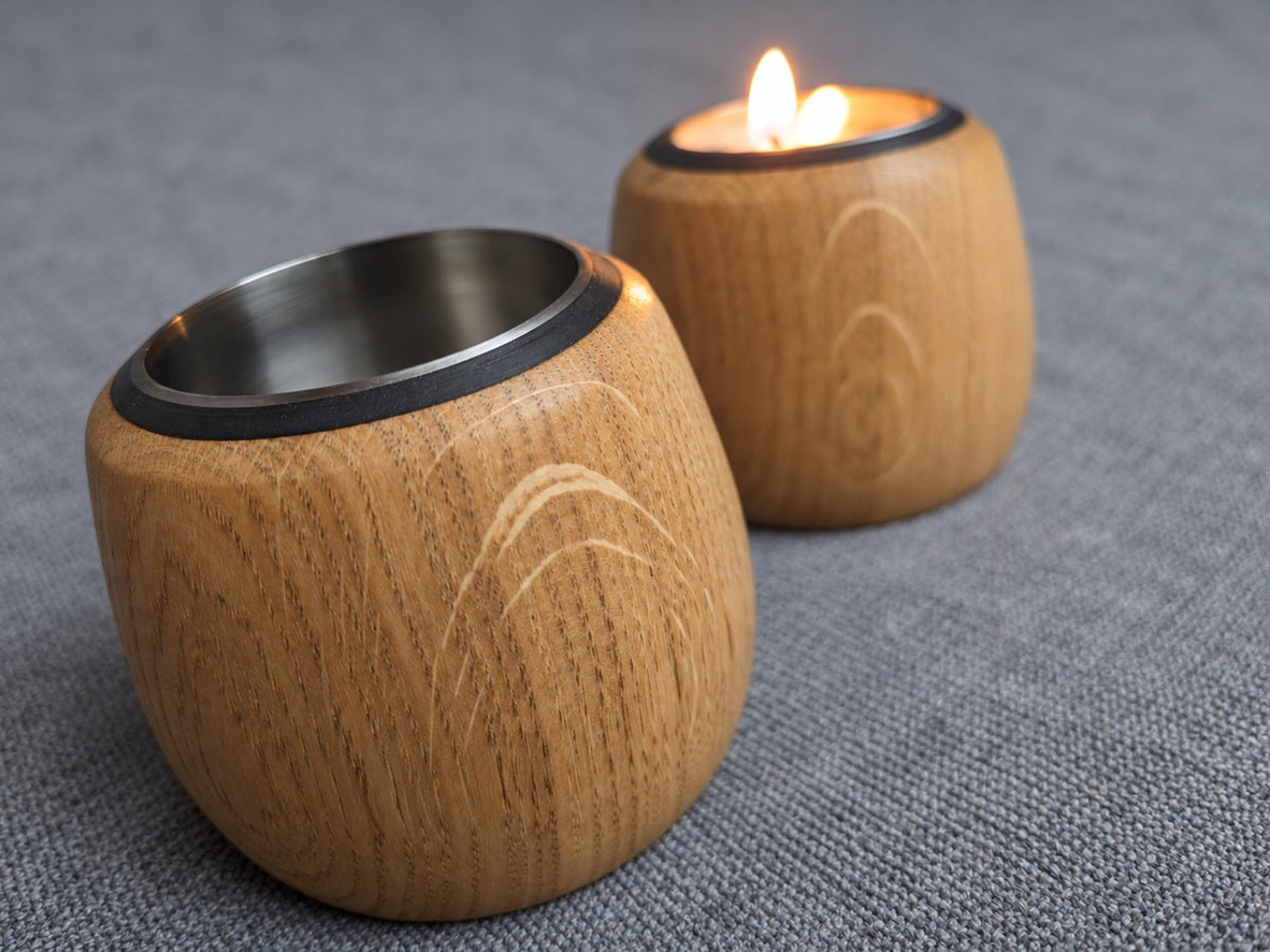 Pair of oak tealight holders with a candle lit in the rear holder and pale flecking in the foreground grain