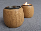Oak tealight holders on grey fabric, showing the natural grain and a lit candle behind