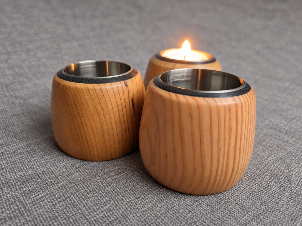 Mixed wood tealight trio on grey fabric with a lit holder behind two unlit holders