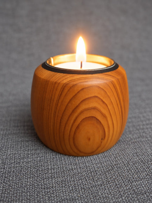 Lit yew tealight holder showing its rounded shape and curved orange grain
