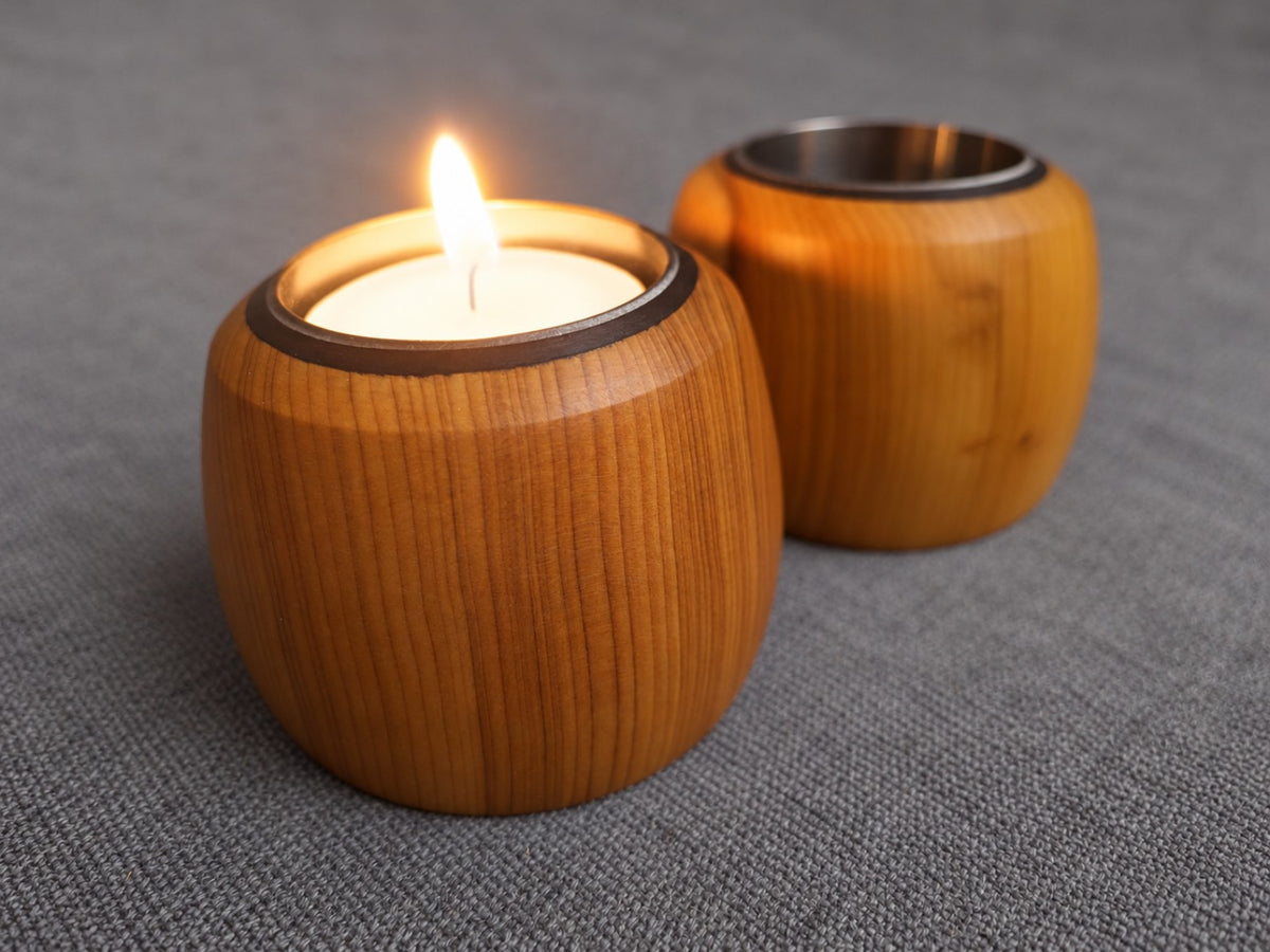 Yew tealight holders on a grey fabric background with a lit candle in the foreground