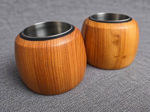 Two handcrafted yew tealight holders showing orange wood grain and stainless steel inserts
