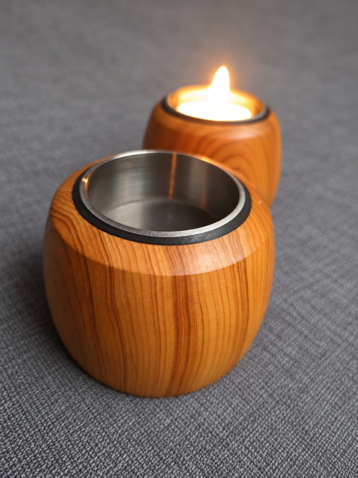 Close view of a yew tealight holder stainless steel insert with a lit holder behind